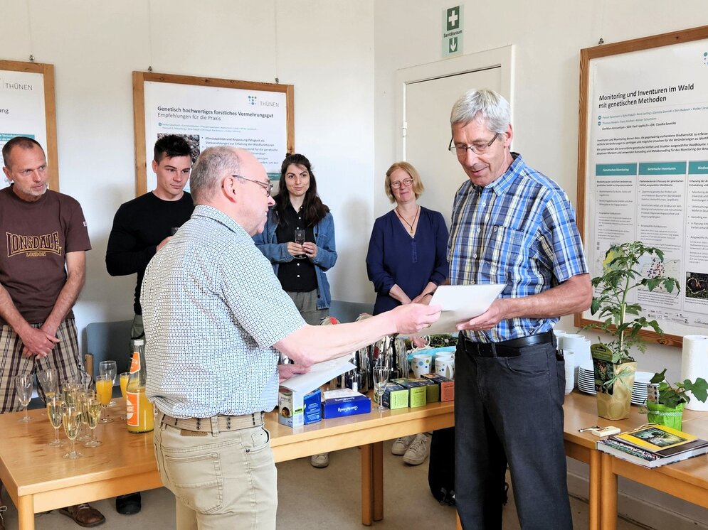 Bernd Degen, links im Bild, übergibt eine Urkunde an Matthias Fladung, rechts. Im Hintergrund stehen weitere Personen.
