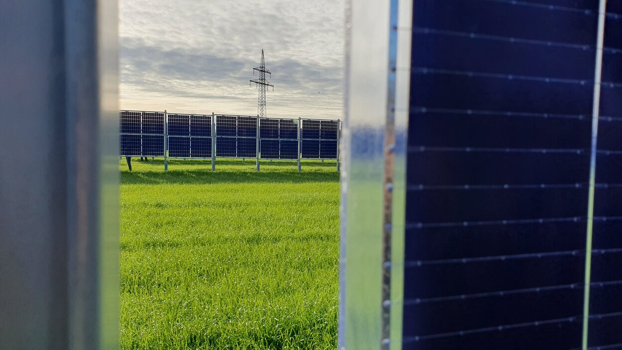 Blick zwischen zwei Agri-PV anlagen auf ein Feld auf dem auch Agri-PV Elemente stehen.