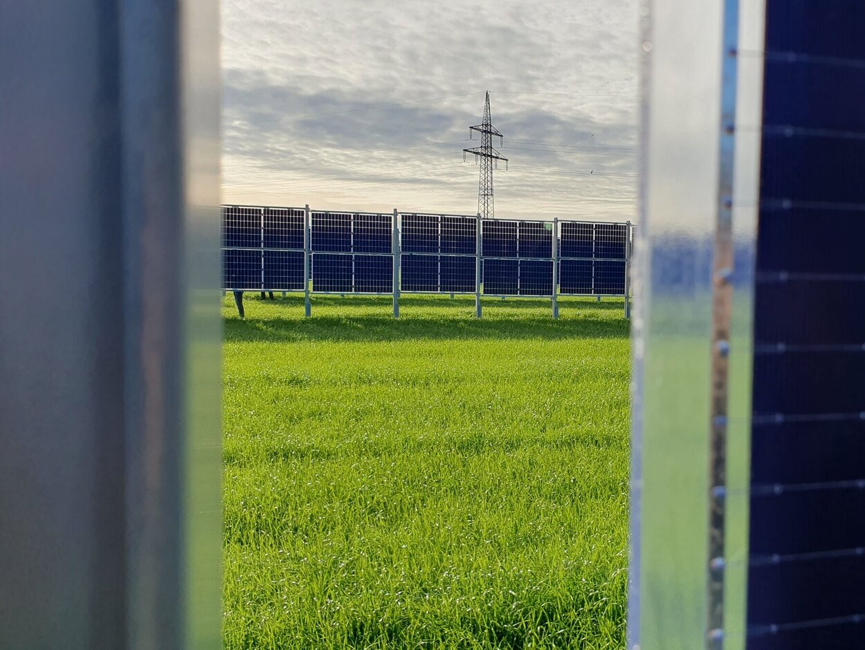 Blick zwischen zwei Agri-PV anlagen auf ein Feld auf dem auch Agri-PV Elemente stehen.