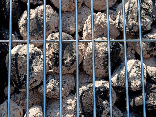 Schon leicht verkohlte Holzkohle unter einem Gitterrost