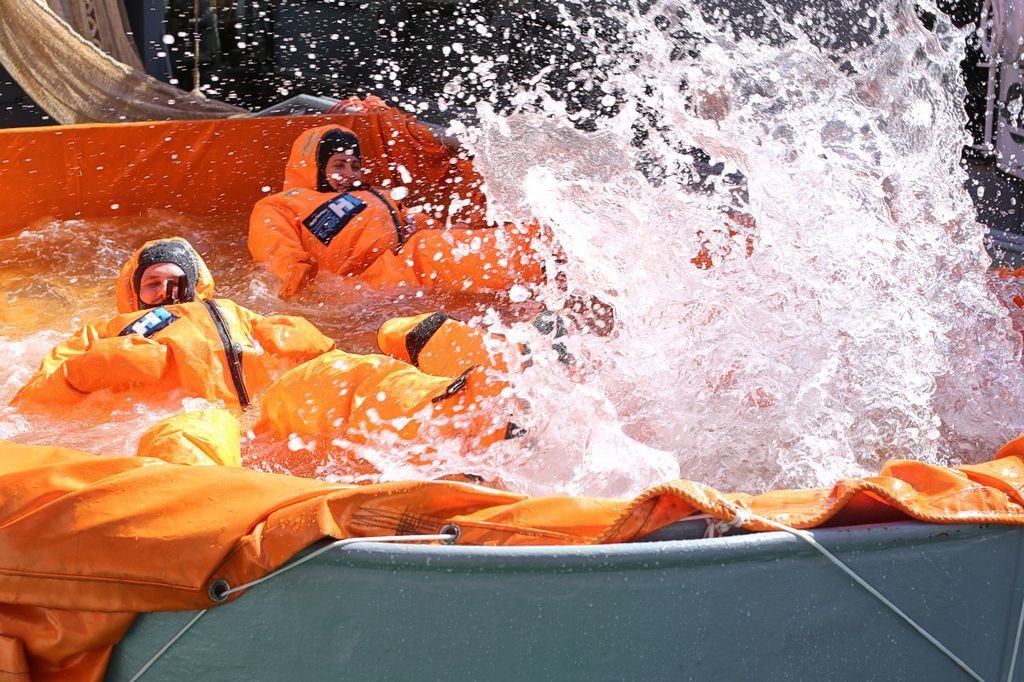 Zwei Personen liegen mit Überlebensanzügen im Wasser, es spritzt viel Wasser hoch