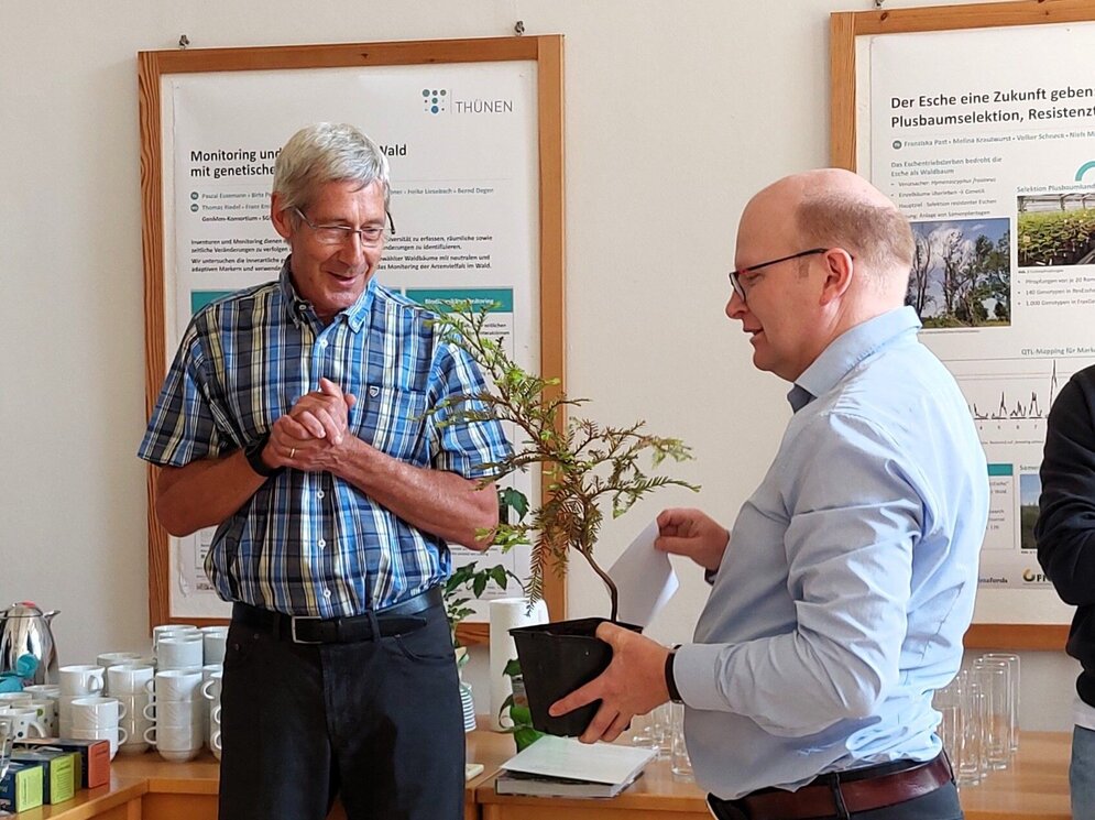 Matthias Fladung ist links im Bild. Ben Bubner, rechts im Bild, übergibt eine Pflanze.