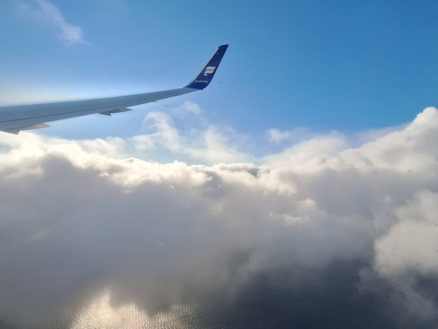 Tragfläche eines Flugzeuges über den Wolken vor blauem Himmel.