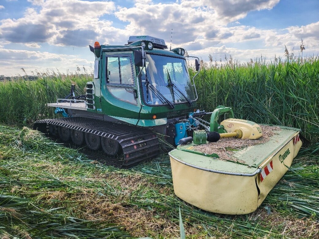 Ein kleiner Trecker mit Kettenantrieb mäht auf einer Moorfläche.