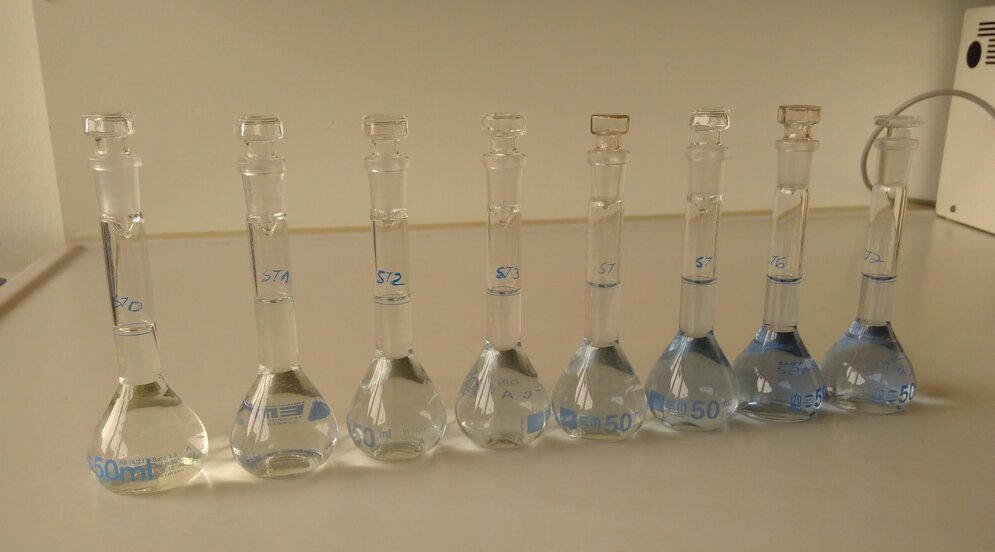 Eine Reihe von Gläsern mit Flüssigkeiten unter einem Abzug, die schwach in verschiedenen blautönen gefärb sind. .