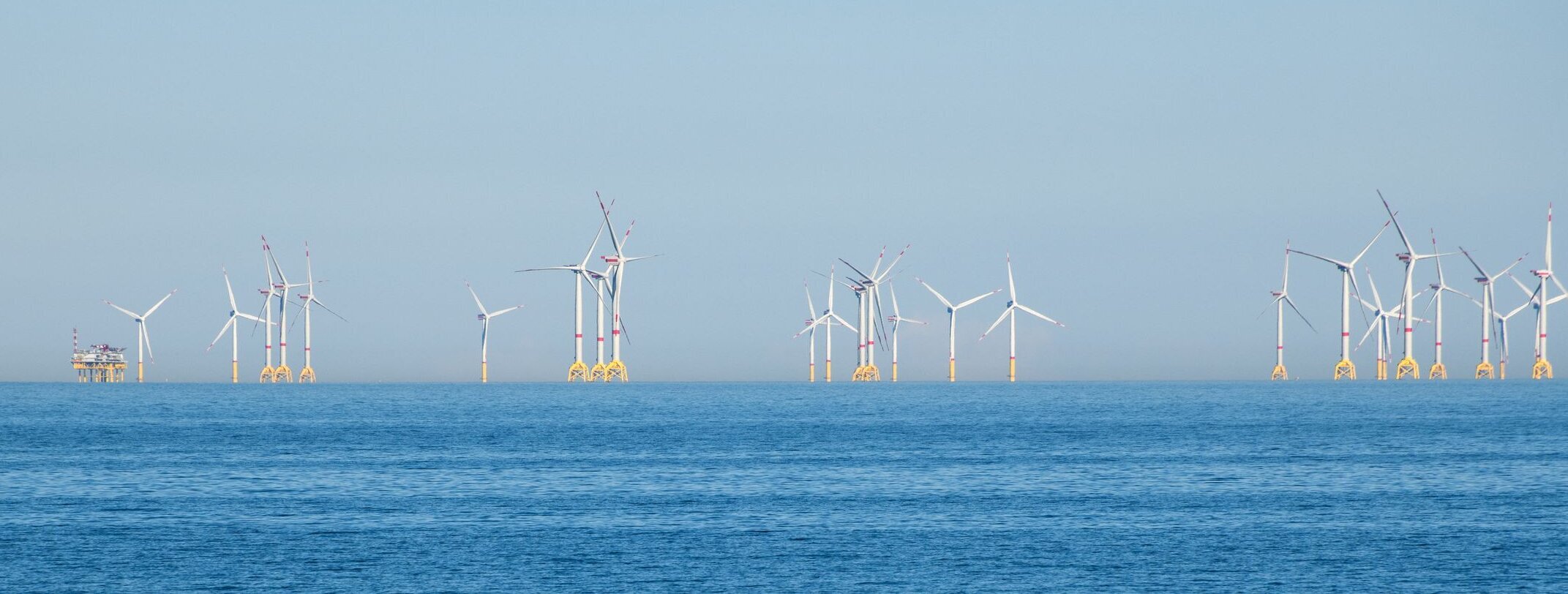 Mehrere Windkrafträder auf offener See mit einer Versorgungstation