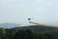 Ein Hubschrauber fliegt über ein Waldgebiet und verstreut Kalk.