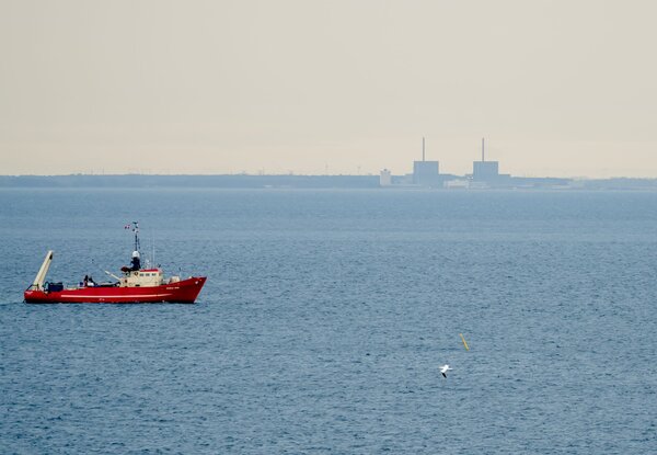 Ein roter Fischkutter fährt im Öresund in Sichtweite des Atomkraftwerks Barsebäk entlang.