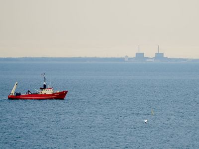 Ein roter Fischkutter fährt im Öresund in Sichtweite des Atomkraftwerks Barsebäk entlang.