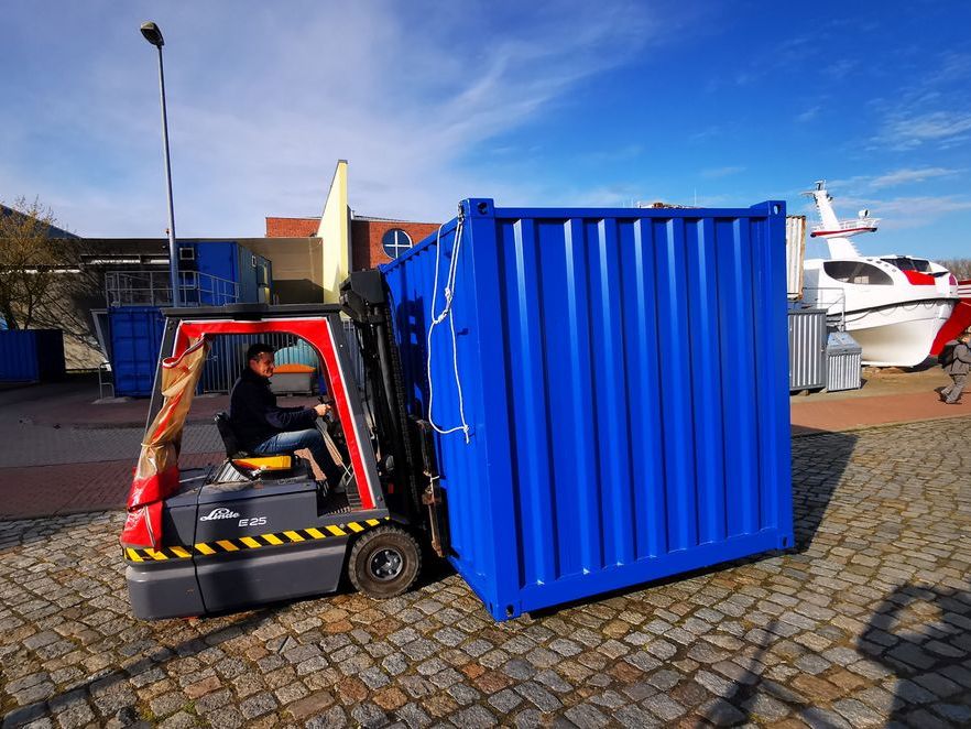 Ein blauer Container wird mit einem Hubwagen angeliefert