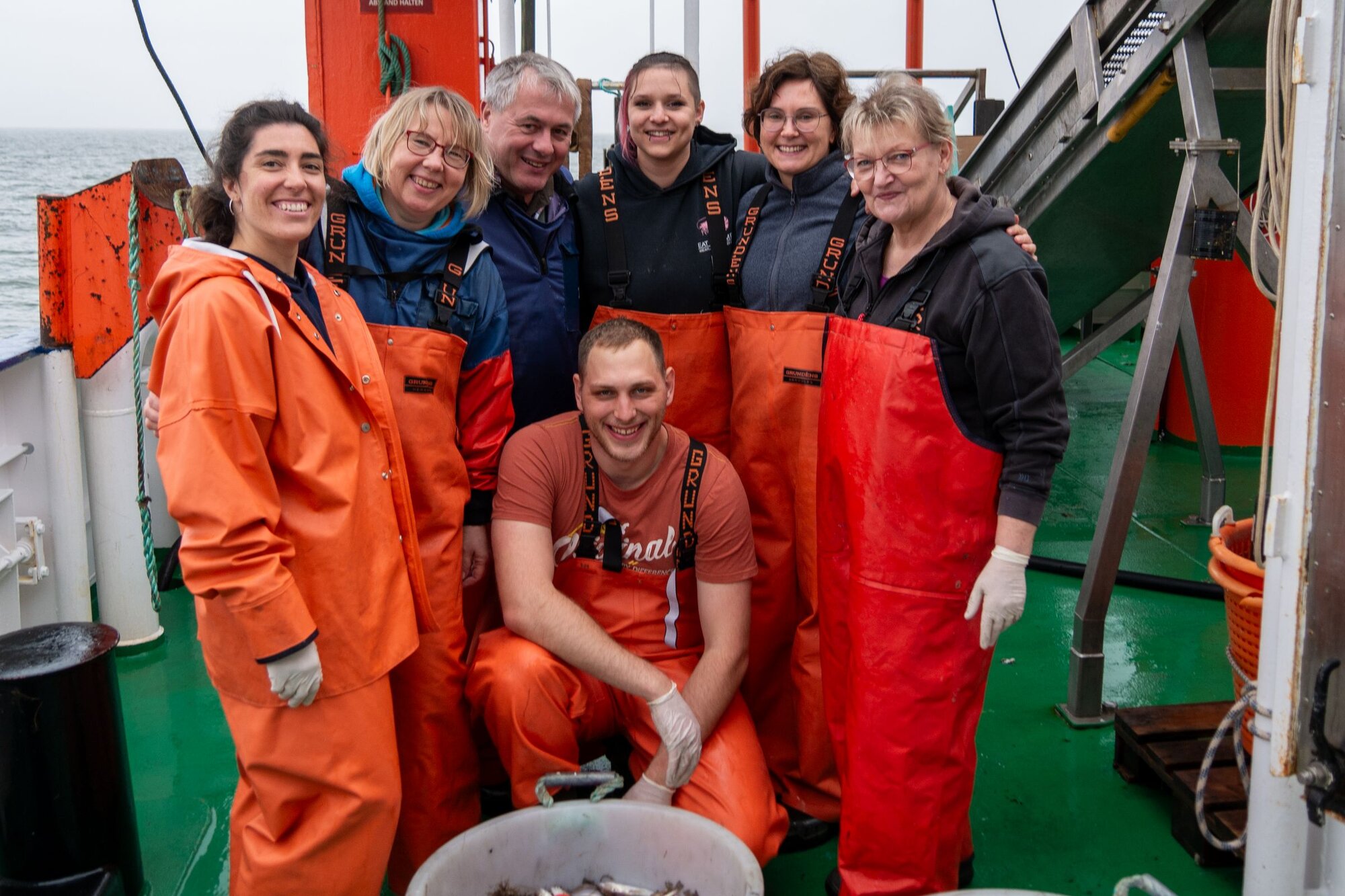 Die vollzählige wissenschaftliche Crew. Sieben Personen stehen in Ölzeug an Deck.