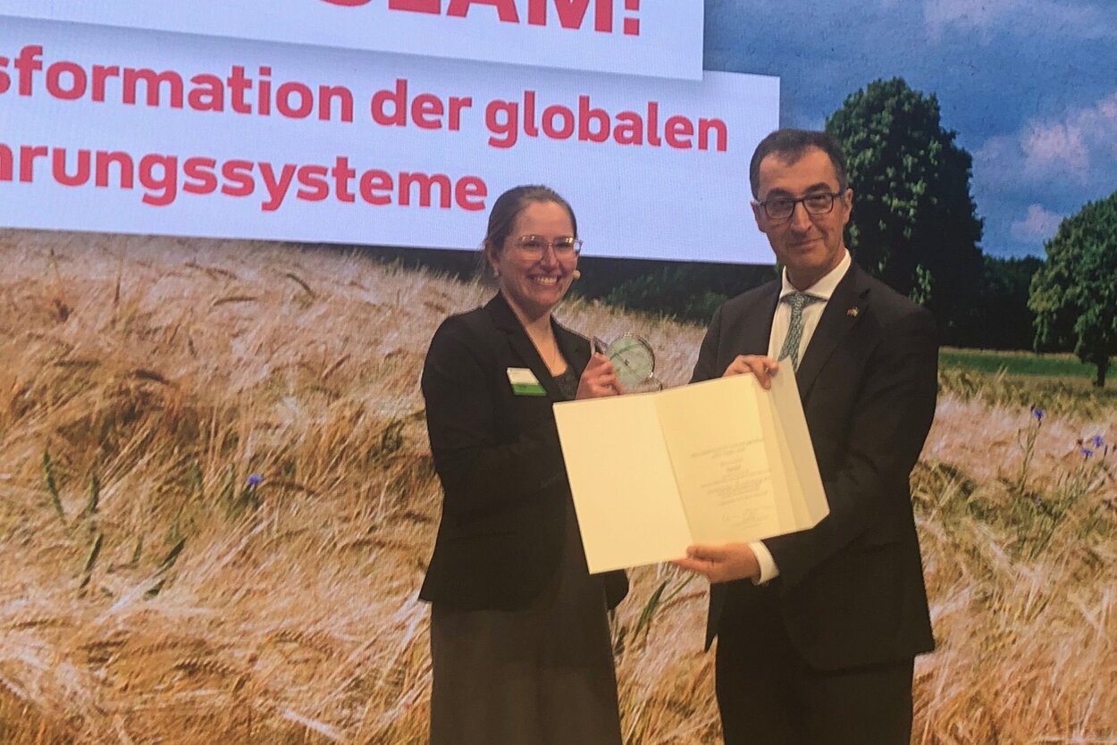 Federal Minister Cem Özdemir presents the winner of the GFFA ScienceSlam, Lia Orr, with the winner's award.