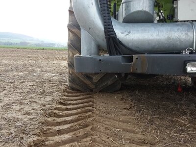 A tractor drives across a field, leaving deep tire tracks behind.