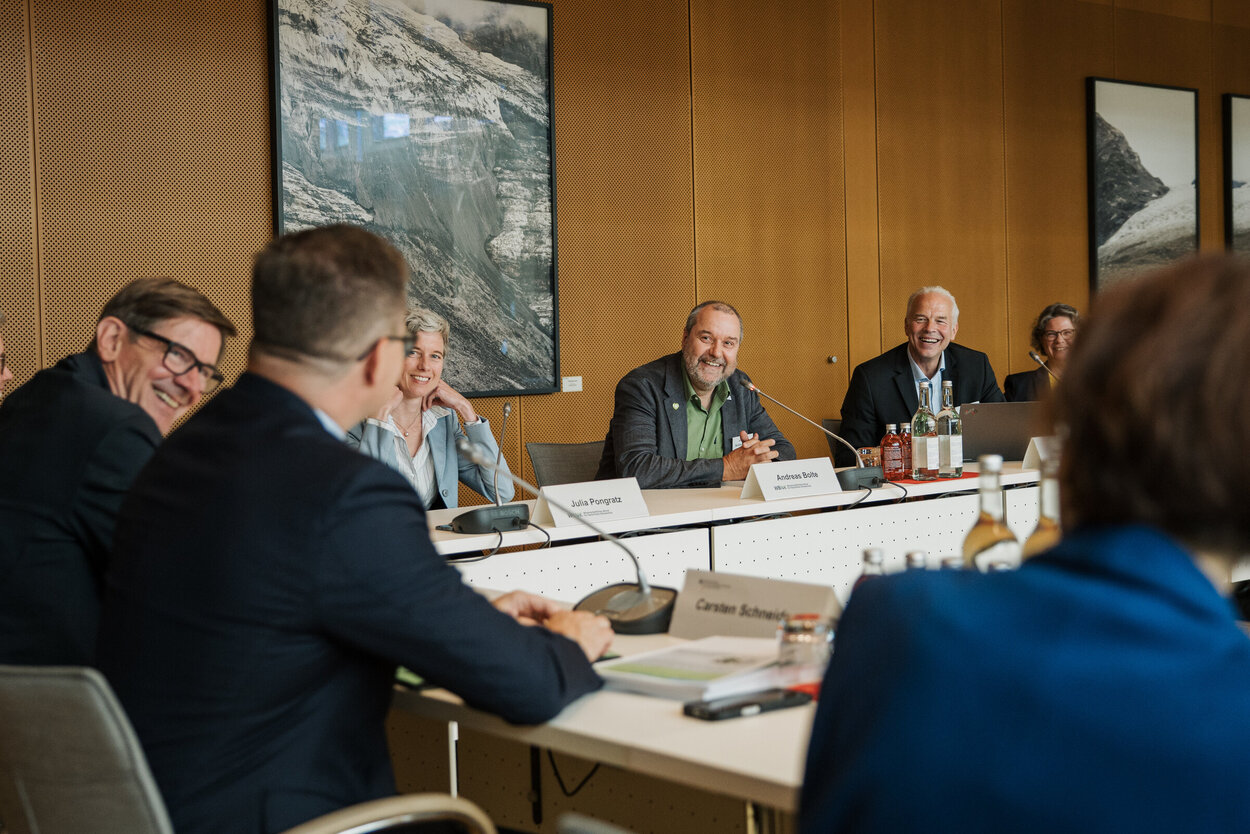 Mehrere Personen sitzen um einen Tisch in U-Form.