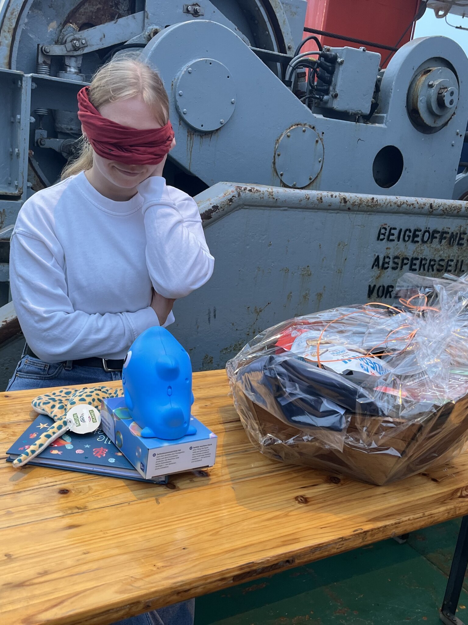 A person sits blindfolded in front of a table with many farewell gifts.