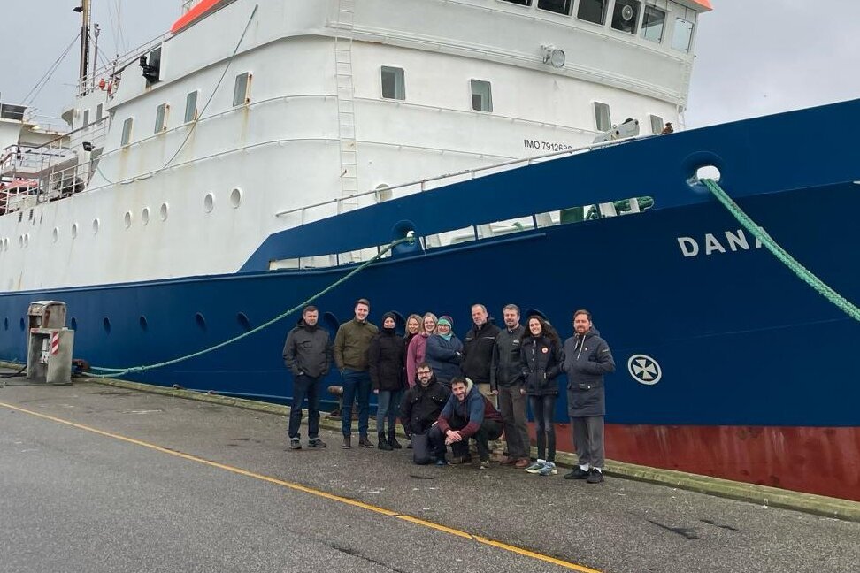 Gruppenfoto nach Ende der Reise: 12 Personen stehen vor dem Bug der Dana.
