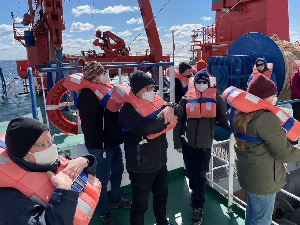 Mehrere Personen mit Rettungswesten stehen auf dem Deck