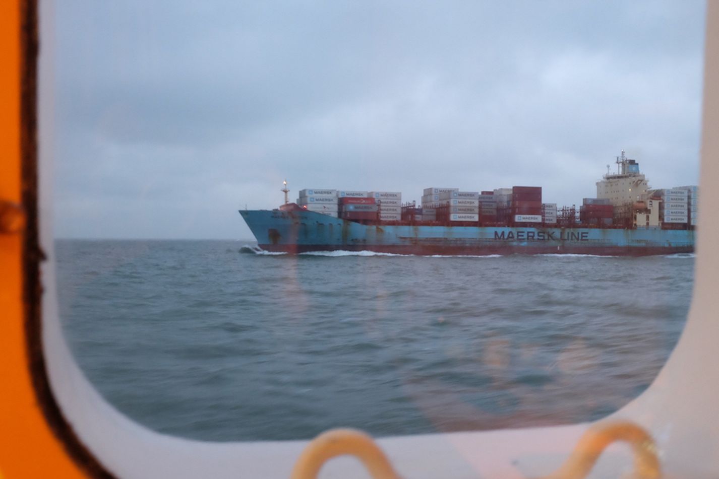 Blick aus dem Schiffsfenster auf eine vorbeifahrendes Containerschiff
