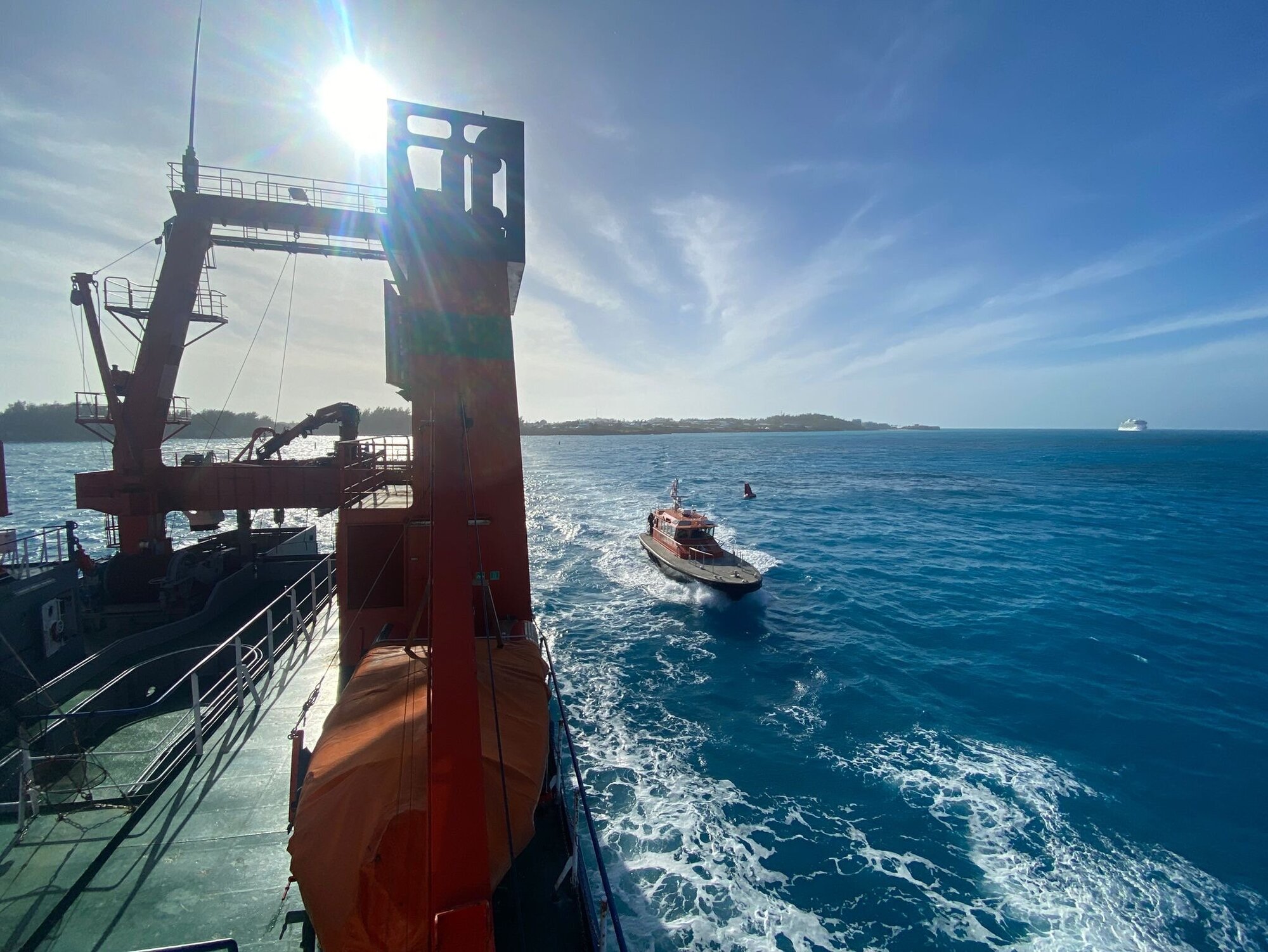 Das Heck der Walther Herwig III mit einem über das mehr wegfahrenden viel kleinerm Boot. Die Sonne strahlt vom Himmel.