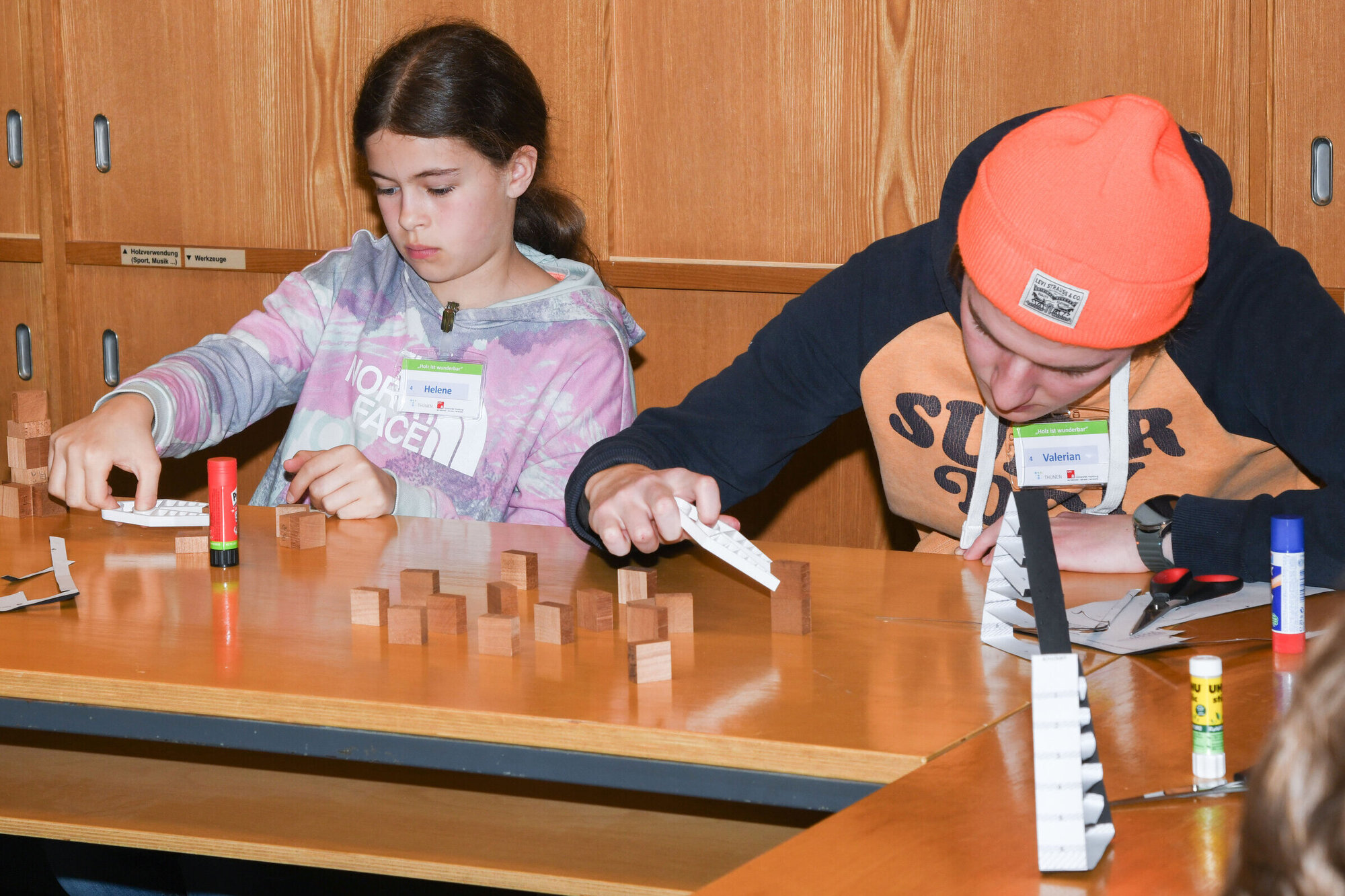 Zwei Kinder arbeiten konzentriert an einem Tisch mit Holzbausteinen und Bastelmaterialien.