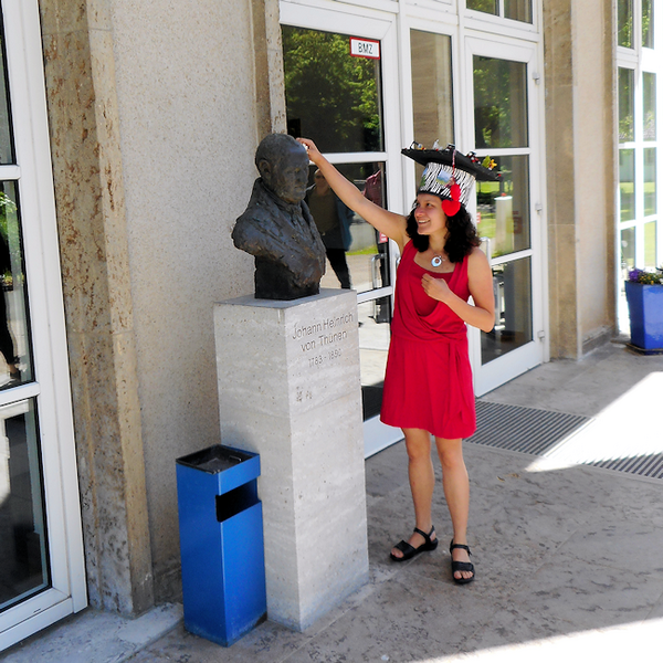 Viridiana Alcántara Cervantes mit Doktorhut an der Büste von Johan Heinrich von Thünen vor dem Forum des Thünen-Institutes in Braunschweig