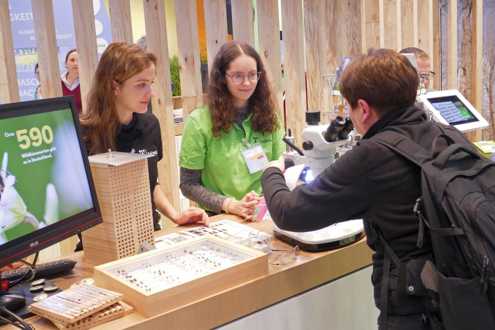Eine Besucherin steht am Thünen-Stand und blickt in ein Mikroskop.