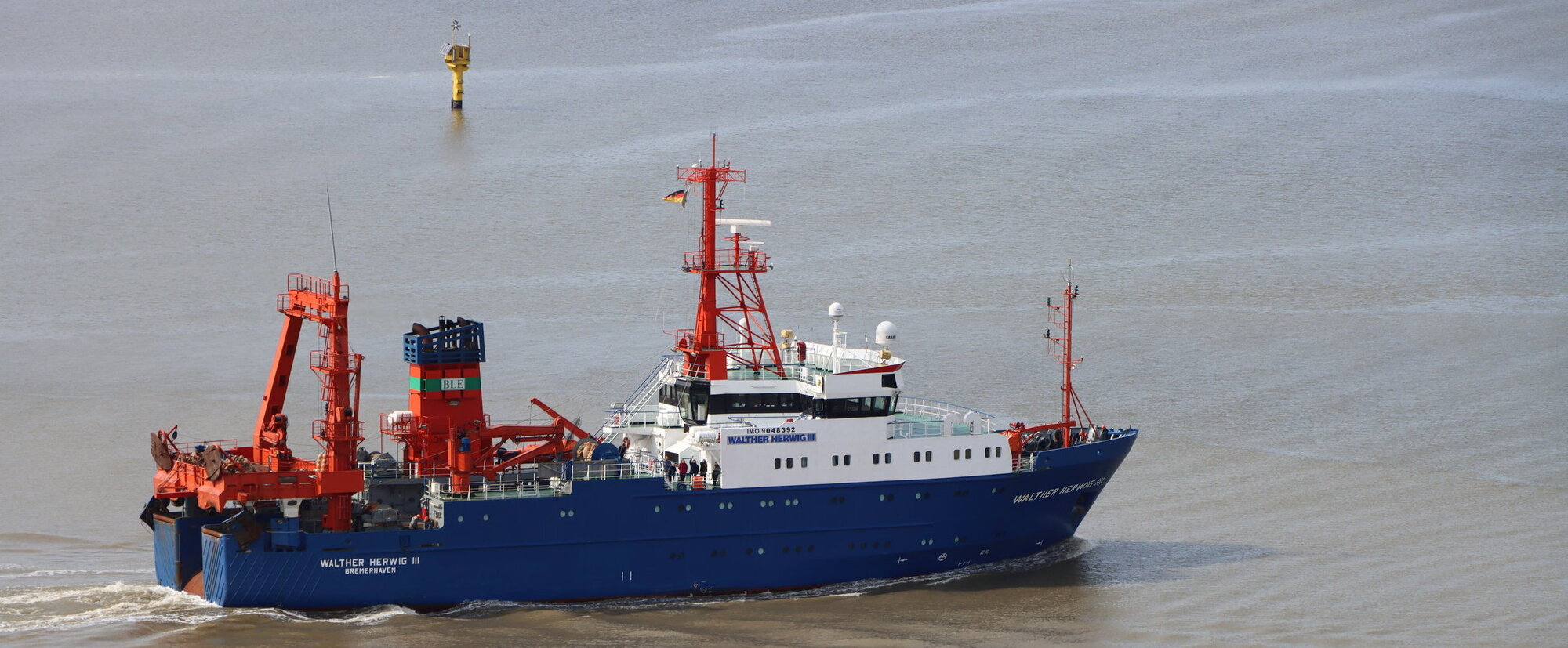 The ship photographed from the side. It is painted blue (hull), orange (superstructure), and white (bridge).