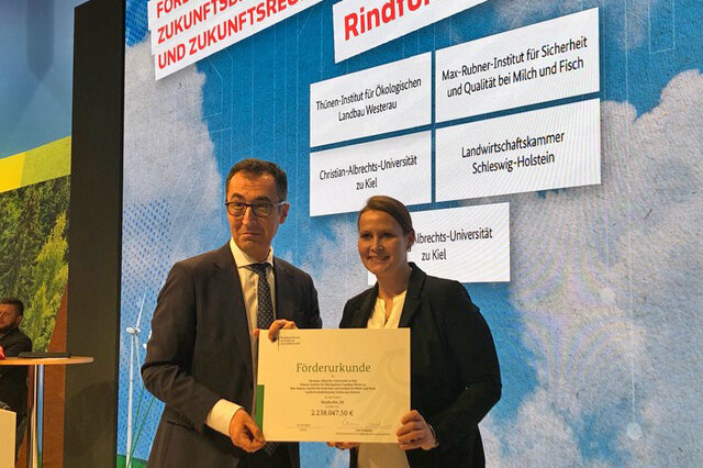 Auf der Bühne der BMEL-Halle überreicht Bundesminister Cem Özdemir den Förderbescheid für das Verbundprojekt RindForNet_SH