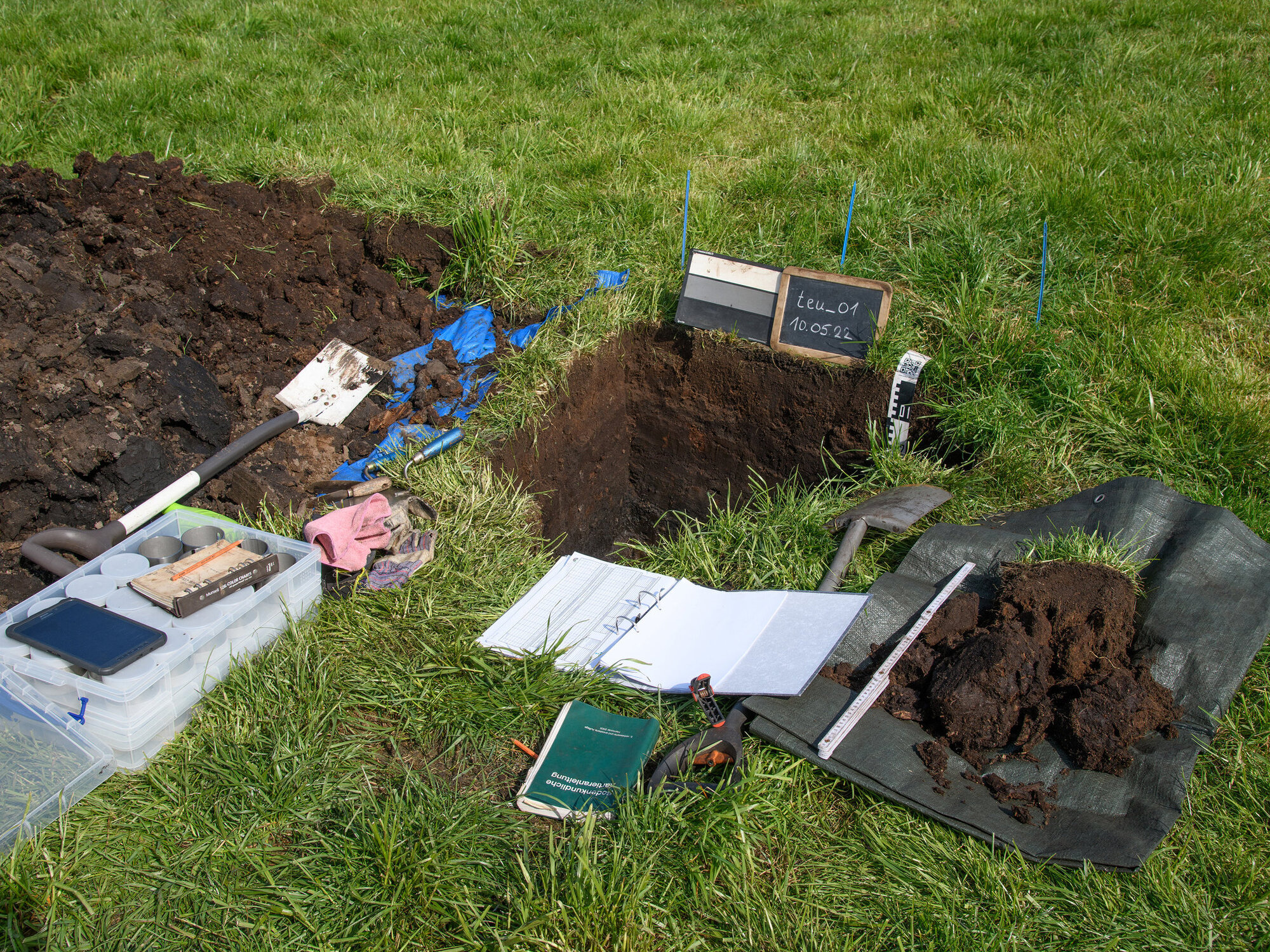 A pit has been dug in a meadow and paper and a spade are ready and waiting.