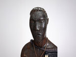 A bust carved from black wood with many decorations on the face.