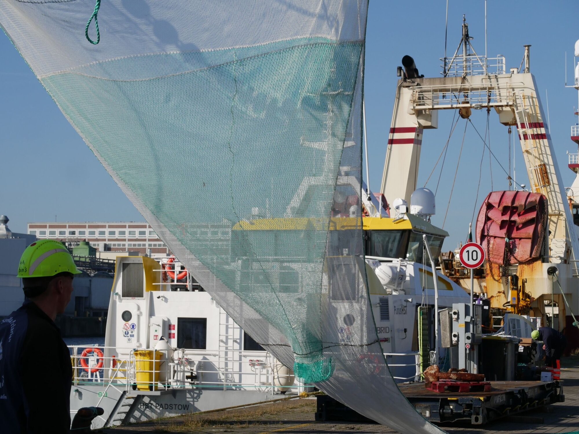 Das grüne Innenleben ist das Siebnetz mit einer Auslassöffnung unten. Siebnetz im Vordergrund mit Schiffaufbauten im Hintergrund.