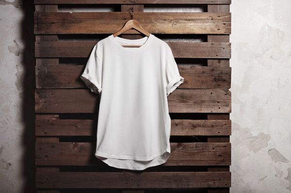 Ein weißes T-Shirt hängt an einem Holzbügel an einer dunklen Holzpalette