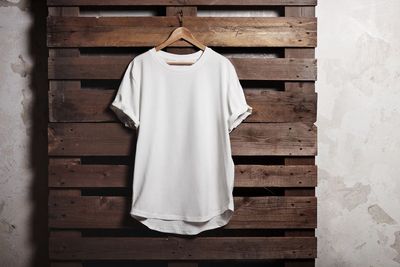 Ein weißes T-Shirt hängt an einem Holzbügel an einer dunklen Holzpalette