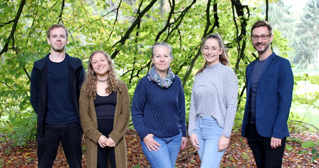 Gruppenfoto mit Alexander Fendel, Virginia Zahn, Susanne Jelkmann, Alice-Jeannine Sievers, Dr. Tobias Brügmann (von links nach rechts). Im Hintergrund sind grün belaubte Zweige einer Rotbuche.