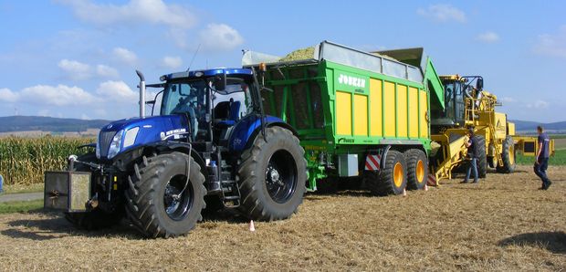 Traktor mit Anhänger, dahinter ein Maishäcksler auf dem Feld