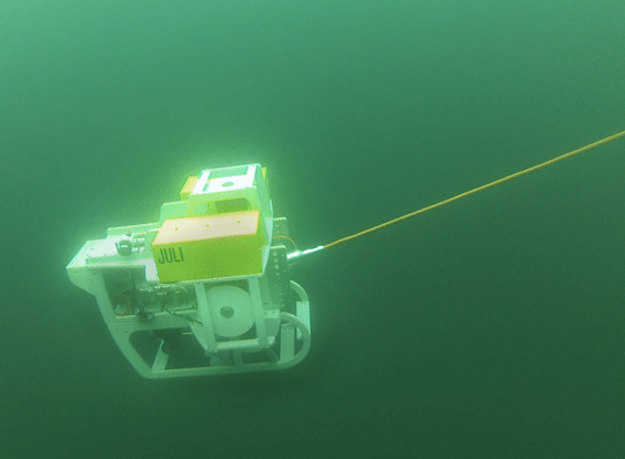 Das Foto zeigt ein Unterwasserfahrzeug, das hinter einem Schiff geschleppt wird und durch Veränderung der Anströmung auch gelenkt werden kann. Mit seiner Kamera kann es das Verhalten von Fischen im Netz dokumentieren. 