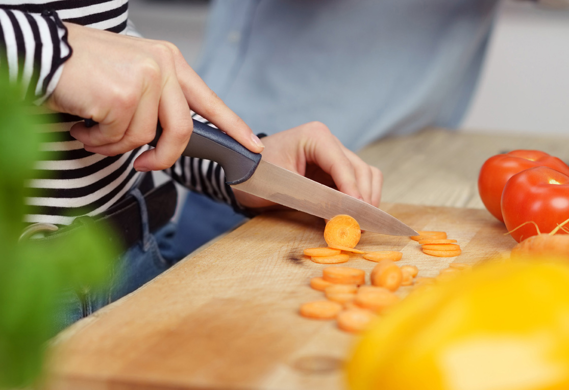 Mit einem Messer wird eine Möhre in Scheiben geschnitten
